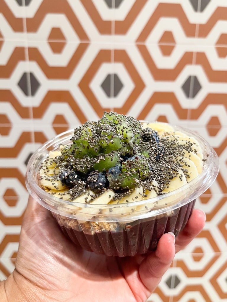 A hand holding a smoothie bowl from Berries and Bowls, which is a shop located in Bethesda, Maryland