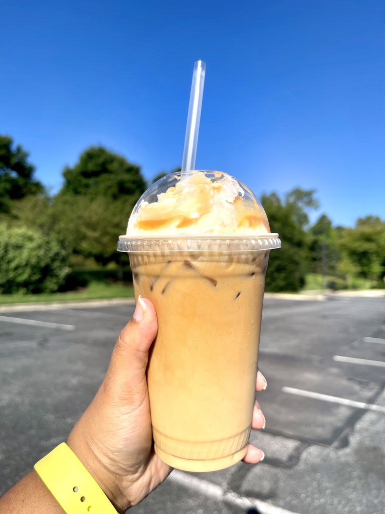 A hand holding a coffee drink from PJ's Coffee in Bowie, Maryland. The drink is called Caramel Cold Creme.