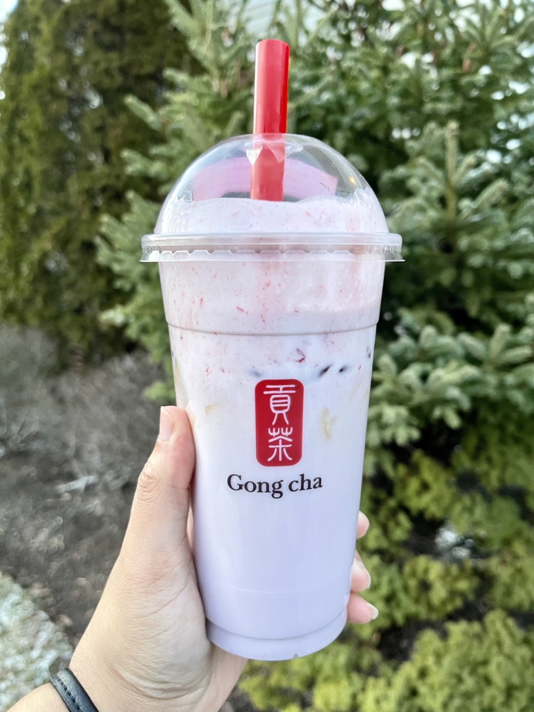 A hand holding a bubble tea drink from Gong cha. The drink is called Taro Coconut Milk Tea.