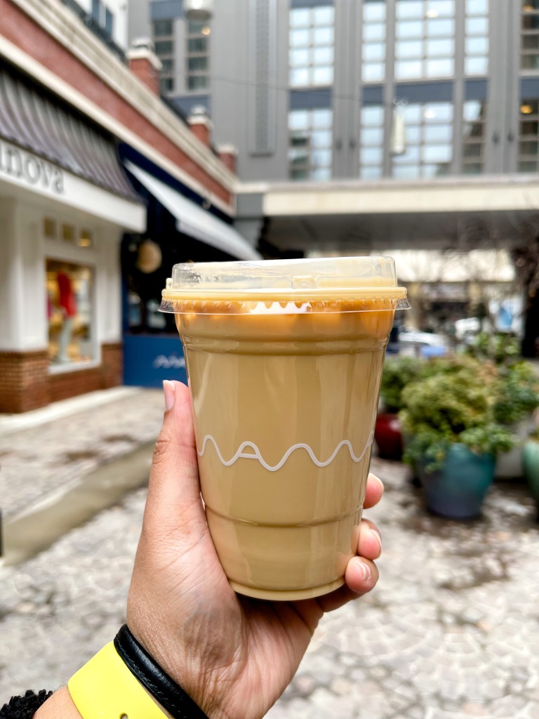 A hand holding an iced honey lavender latte from maman, a cafe located in Bethesda, Maryland